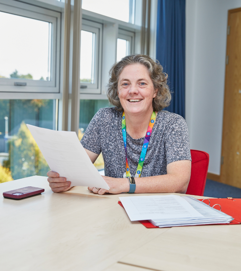 Smiling woman with curly gray hair holding documents at desk