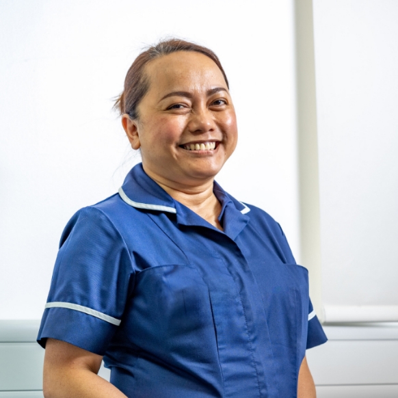 Smiling woman in blue nurse uniform with white trim against light background.