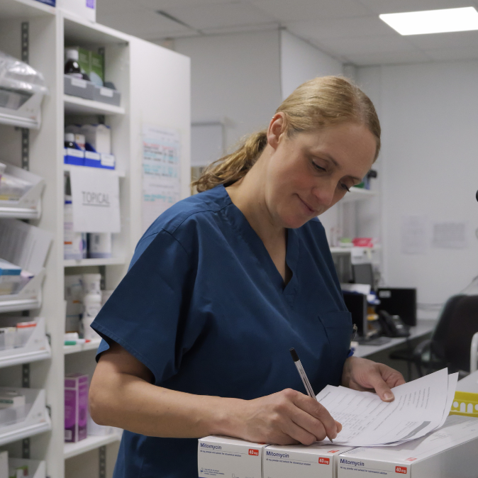 Female healthcare worker in scrubs writing in a pharmacy