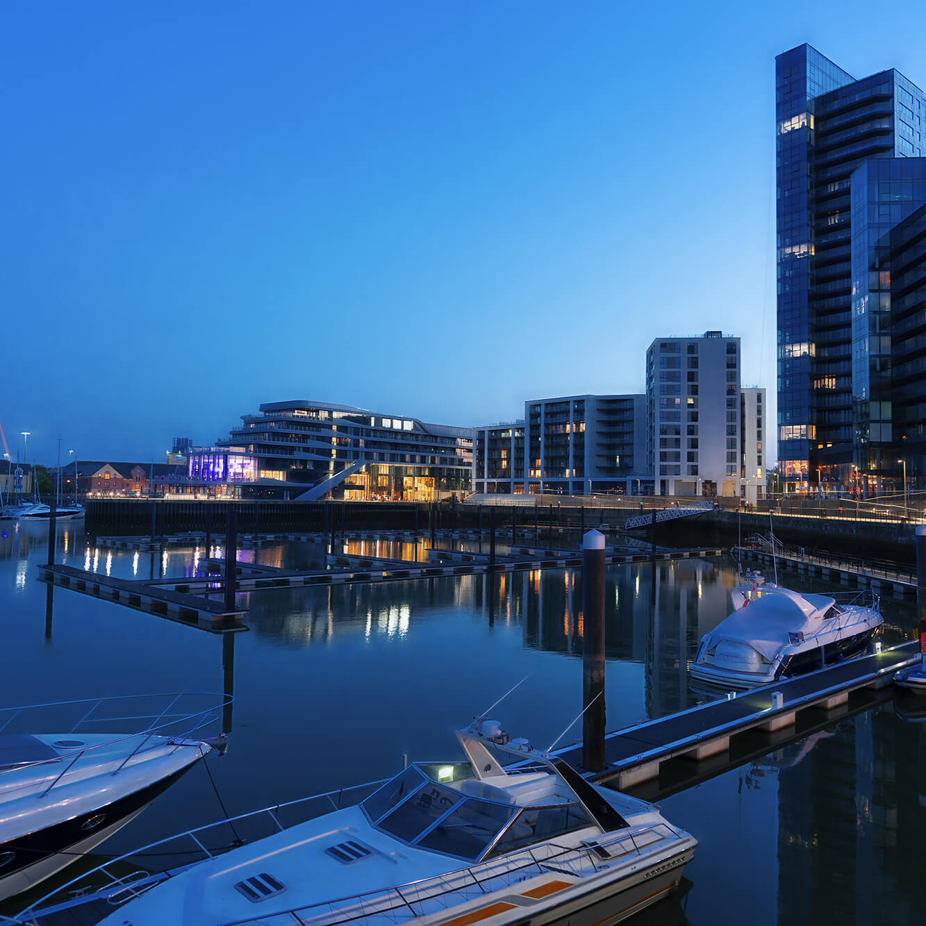 Twilight marina with yachts and modern buildings under clear blue sky.