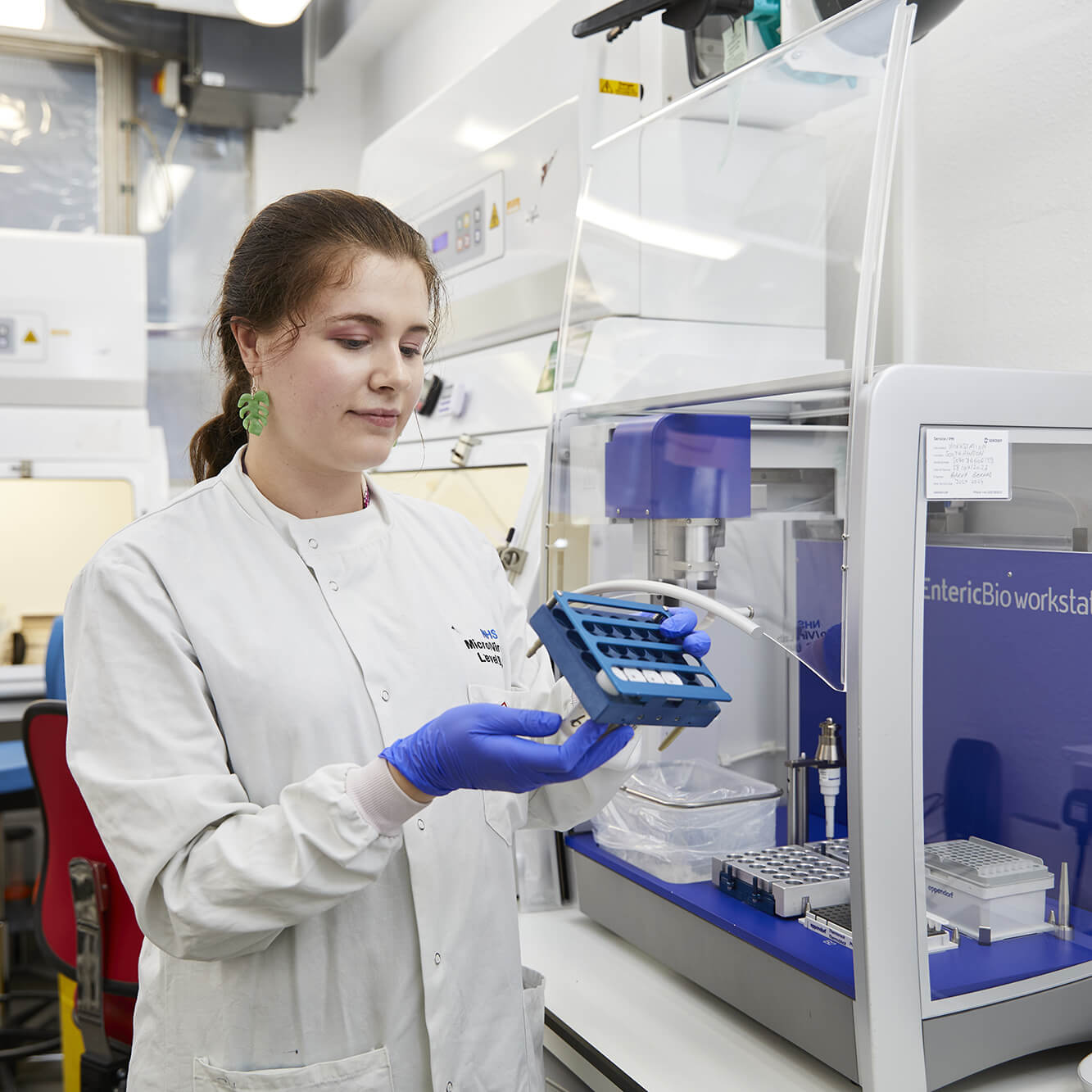 Female scientist in lab coat examining samples beside open lab workstation.