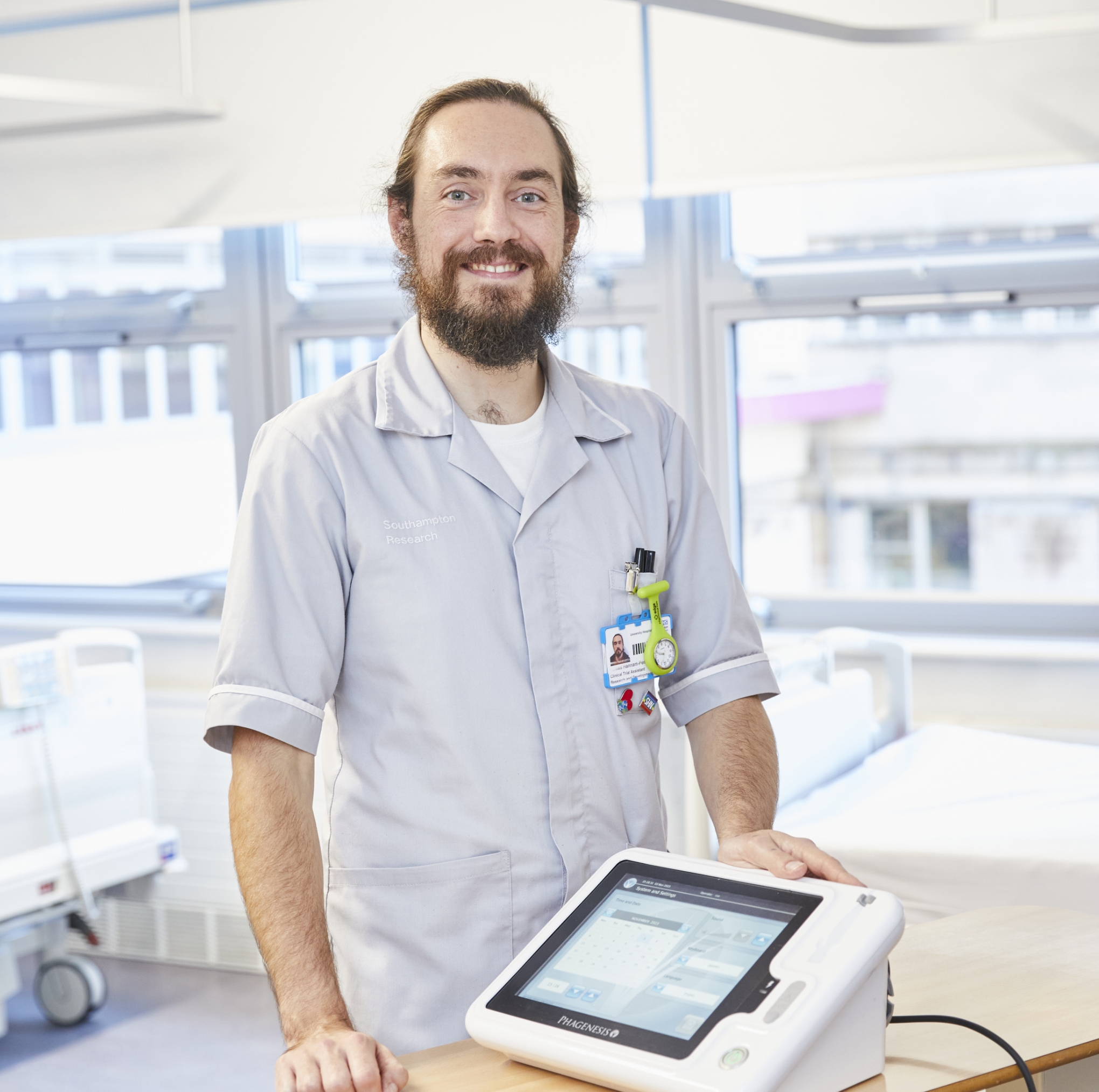 Smiling male healthcare worker in grey uniform beside medical device on trolley.