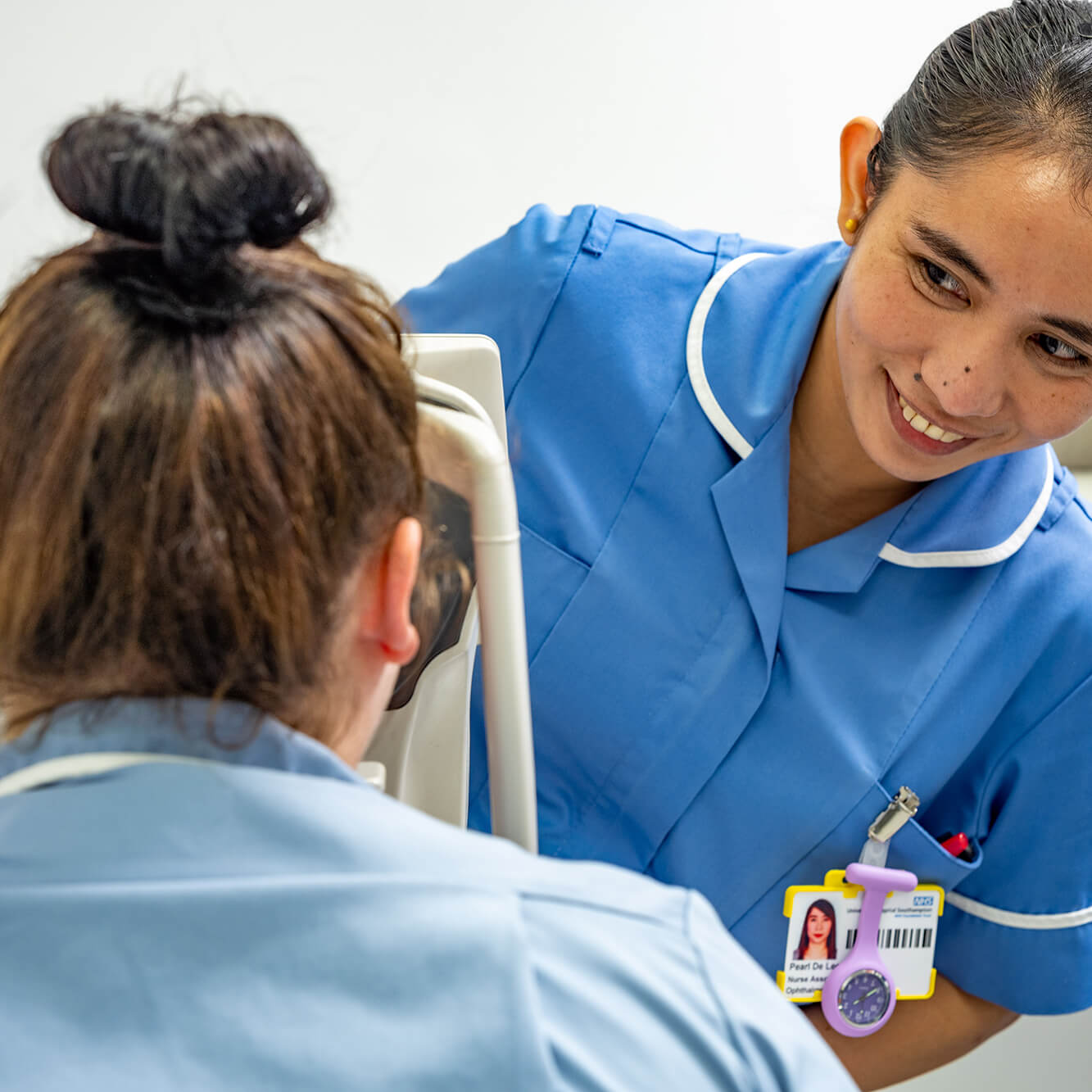 Smiling nurse in blue uniform assisting patient in medical chair.