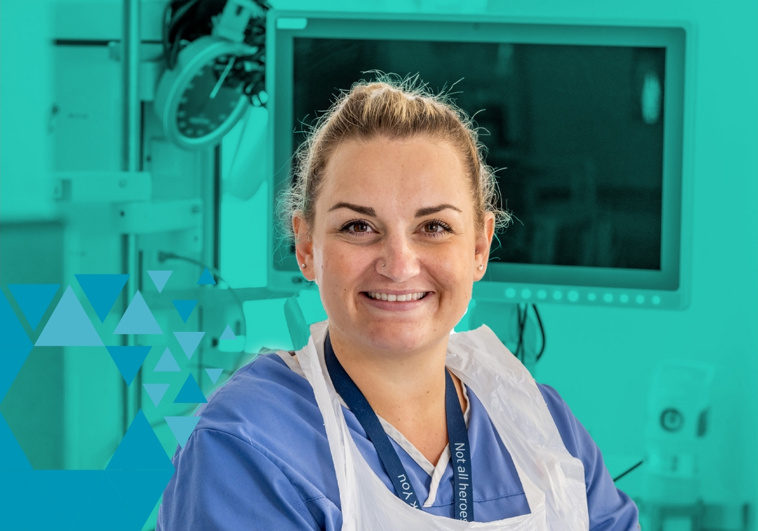 Smiling nurse in blue scrubs and lead apron in a hospital room.