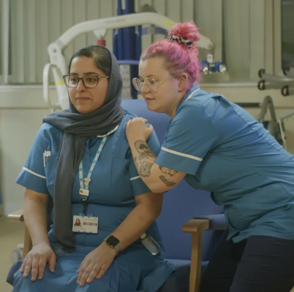 Two nurses in uniform sharing a supportive moment.