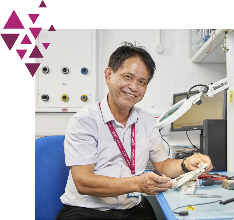 Elderly man working on electronics under a magnifying lamp