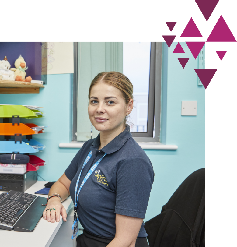 Woman in blue polo shirt at desk with computer, looking at camera