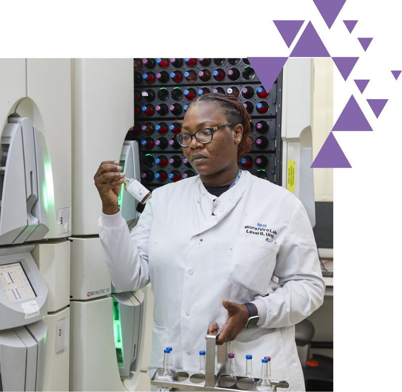 Female scientist examining a vial in a lab with test tubes in background