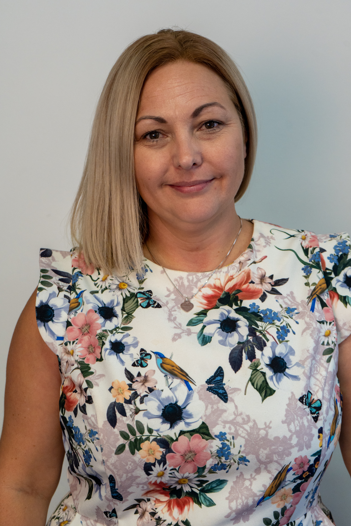 Smiling woman with blonde hair in floral dress with butterflies and birds.