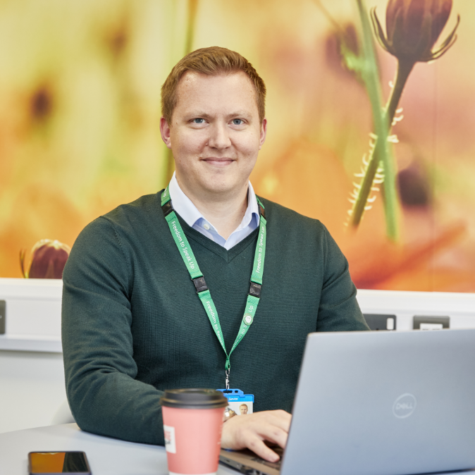 Man in green sweater working on laptop in floral office
