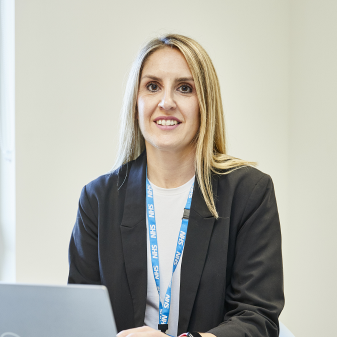 Woman in blazer smiling at desk with laptop